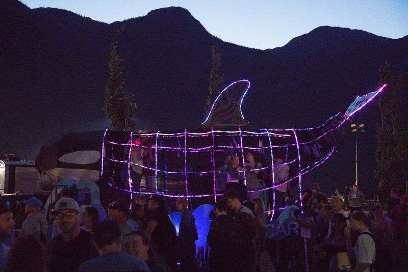 The Orcar, a community-built orca sculpture, outlined in purple lights above a festival crowd at night